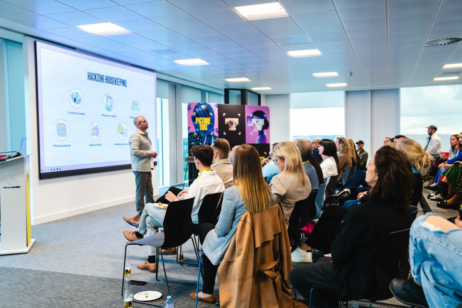 a crowd of people watching a man talking in front of a presentation